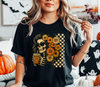 Person wearing a black t-shirt with a retro groovy skeleton design with daisies and a spooky coffee drink