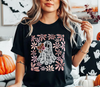 Person wearing a black t-shirt with a ghost and floral design, sitting in a room decorated for Halloween.