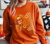 A close-up of a model wearing an orange sweatshirt featuring Boho Floral Skeleton DTF transfer! This vibrant design features a cool skeleton in sunglasses with a groovy floral hairstyle and a retro checkered background.