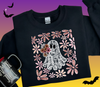 A detailed close-up showing a black t-shirt featuring a spooky cute lace ghost DTF transfer holding a daisy bouquet, with a retro floral border.